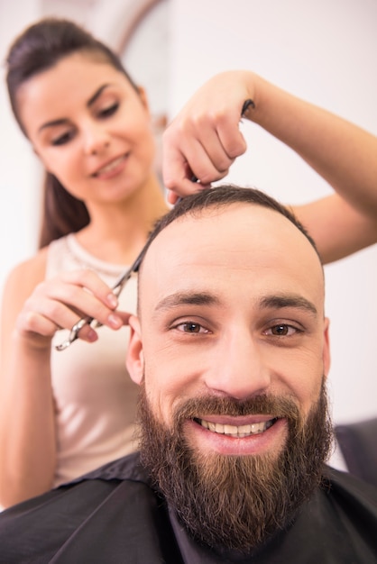 Vrouwelijk kapper scherp haar van glimlachende mensencliënt.