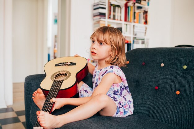 Vrouwelijk kind dat binnen thuis gitaar houdt