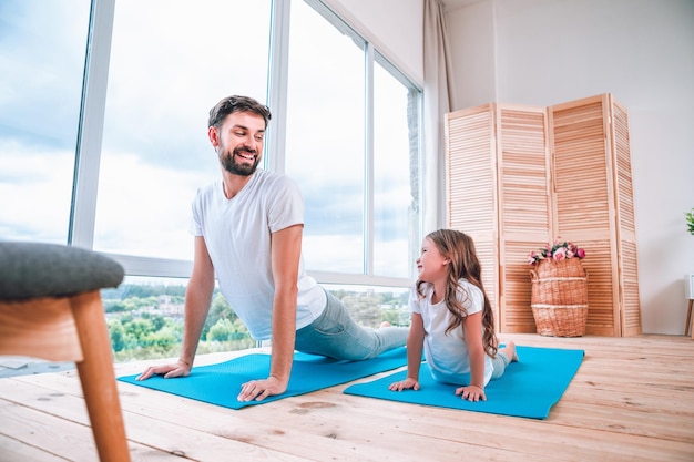 Vrouwelijk kind en man die yoga doen op yogamatten die elkaar thuis aankijken
