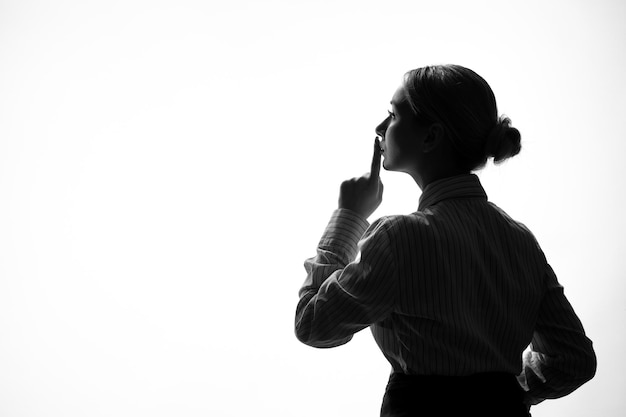 Vrouwelijk silhouet in strikte kleding vragen om stil te zijn schaduw terug verlichte witte achtergrond young