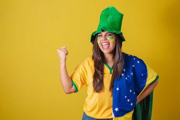 Vrouwelijke aanhanger van het WK 2022 van Brazilië, gekleed in typische fanoutfit om naar het spel te gaan, de vlag van Brazilië en feesten met een groene hoed