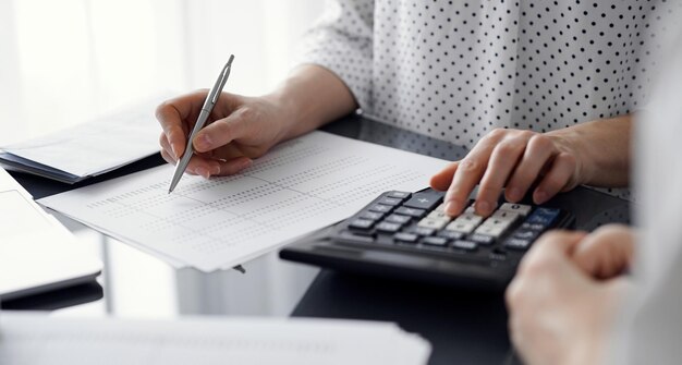 Vrouwelijke accountant die een rekenmachine en een laptop gebruikt bij het tellen van belastingen voor een klant.