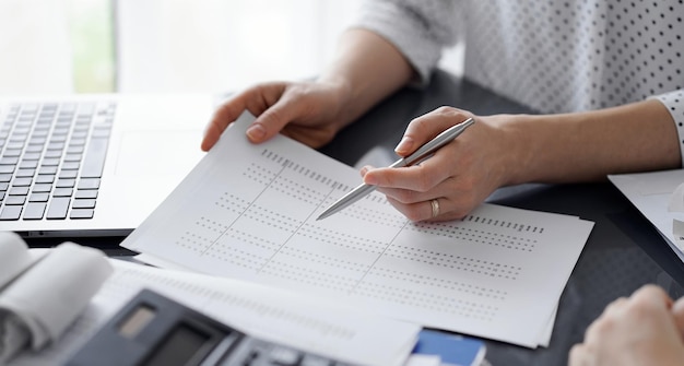 Vrouwelijke accountant die met een pen in controlepapier wijst terwijl ze de resultaten van de belastingtelling uitlegt, close-up. Business audit en financiële concepten