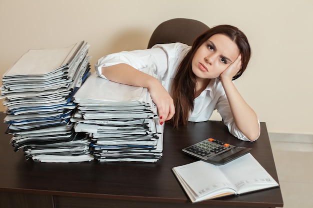 Vrouwelijke accountant knuffelt grote stapels documenten