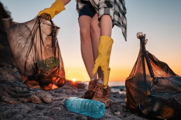 Foto vrouwelijke activiste met twee polyethyleenzakken en een plastic fles op het wilde strand close up of hand low angle view het concept van het schoonmaken van de kust en earth day