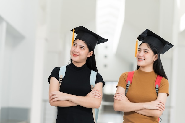 Vrouwelijke afgestudeerden met zwarte hoeden, gele kwastjes, glimlachend en gelukkig op de dag van afstuderen