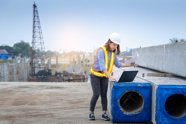 Vrouwelijke architectenleider die met laptop en blauwdrukken werkt op bouwplaats of bouwplaats.