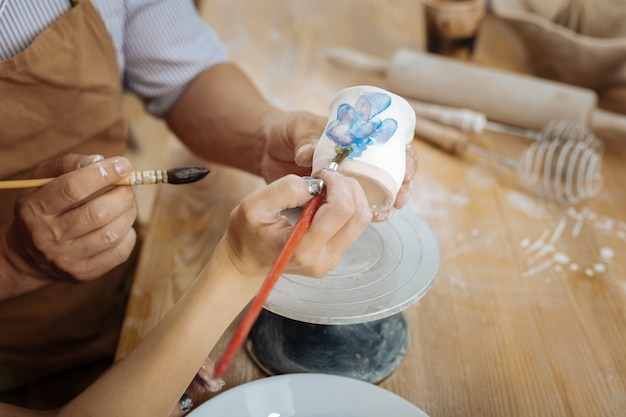 Vrouwelijke artiest. Vrouwelijke artiest met donkere nail art die het druk heeft tijdens het schilderen van bloem op aardewerken beker