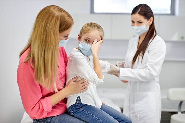 Vrouwelijke arts bloedmonster test van een klein meisje in de kliniek, bang meisje zit met moeder, vrouw technicus bloedtesten maken op kind in het laboratorium van bloed extracties