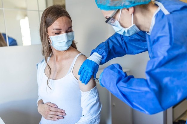 Vrouwelijke arts die Covid-19-vaccininjectie geeft aan jonge zwangere vrouw in gezondheidscentrum. Aanstaande dame wordt geïmmuniseerd tegen coronavirus in de kliniek. Bevolkingsvaccinatie concept