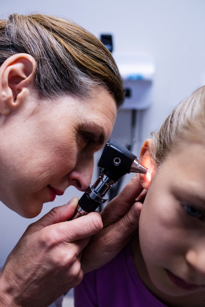 Vrouwelijke arts die geduldig oor met oorspiegel onderzoeken