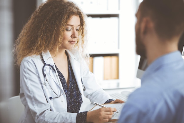 Vrouwelijke arts en mannelijke patiënt bespreken het huidige gezondheidsonderzoek terwijl ze in de kliniek zitten, close-up. Geneeskunde concept.