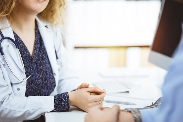 Vrouwelijke arts en mannelijke patiënt bespreken het huidige gezondheidsonderzoek terwijl ze in een zonnige kliniek zitten, close-up. geneeskunde, gezondheidszorg.