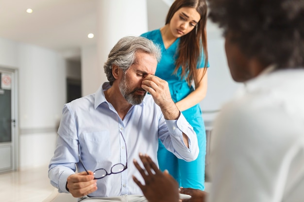 Vrouwelijke arts geruststellend ter ondersteuning van senior volwassen patiënt in het ziekenhuis. Vriendelijke zorgzame jonge vrouw verpleegster of verzorger die oudere gepensioneerde man helpt praten, troost geven, zorgconcept uitdrukken.