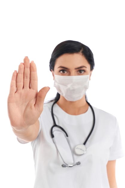 Vrouwelijke arts in medisch uniform en masker met palmstopteken op wit