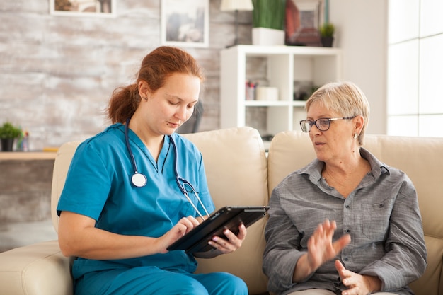 Vrouwelijke arts met behulp van tablet pc en senior vrouw in verpleeghuis.