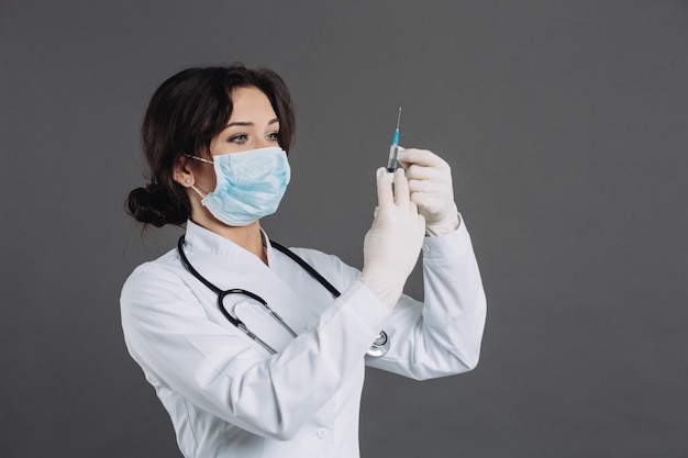 Vrouwelijke arts met stethoscoop in de injectie van de maskerholding, tegengif tegen coronavirus op grijze achtergrond.