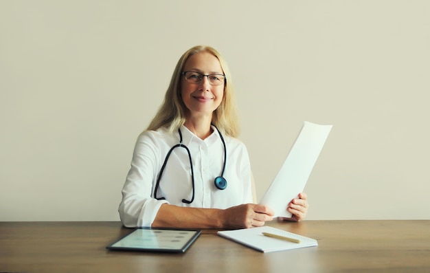 Foto vrouwelijke arts met stethoscoopdocumenten digitale tabletcomputer zit aan het bureau in het kantoor van de kliniek