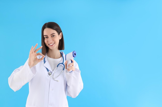 Vrouwelijke arts met thermometerkanon op blauwe achtergrond