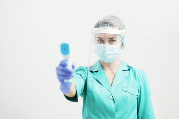 Vrouwelijke arts of verpleegkundige in beschermend masker in het ziekenhuis houdt pyrometer in de hand