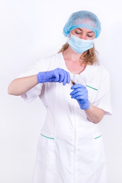 Vrouwelijke arts of verpleegster in een beschermend masker en handschoenen opent een ampul met een vaccin voor injectie...