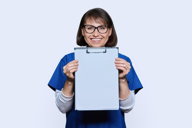 Vrouwelijke arts wijst met de vinger naar blank papier op de clipboard op een witte achtergrond