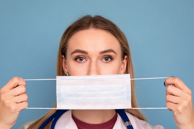 Foto vrouwelijke arts zet een beschermend masker op een blauwe achtergrond