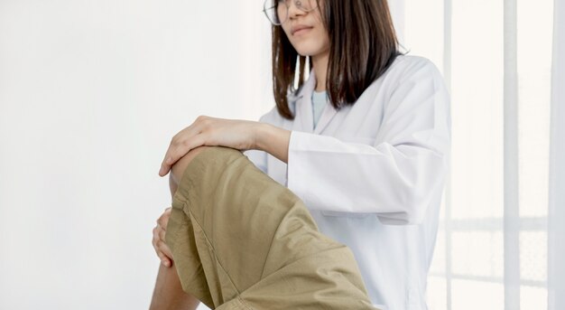 Vrouwelijke artsenhanden die fysiotherapie doen door het been en de knie van een mannelijke patiënt uit te breiden.