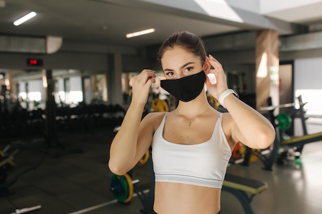 Vrouwelijke atleet met zwart gezichtsmasker heeft een pauze tussen oefeningen in de sportschool