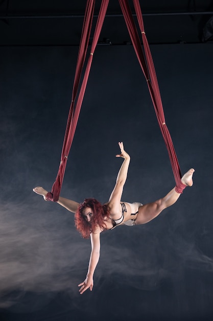 Vrouwelijke atletische, sexy en flexibele luchtcircusartiest met roodharige die in de lucht op de zijde danst.