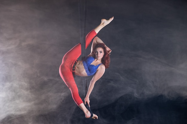 Vrouwelijke atletische, sexy en flexibele luchtcircusartiest met roodharige op luchtbanden op zwarte achtergrond.