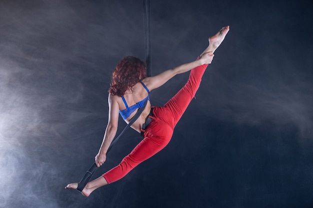 Vrouwelijke atletische, sexy en flexibele luchtfoto circusartiest met roodharige op luchtfoto riemen op zwart.