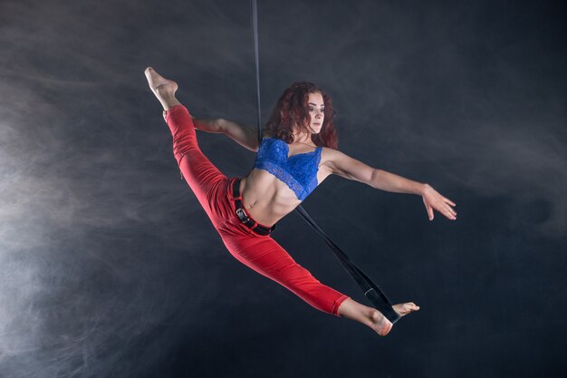 Vrouwelijke atletische, sexy en flexibele luchtfoto circusartiest met roodharige op luchtfoto riemen op zwart.