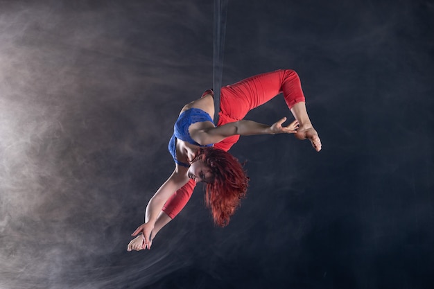 Vrouwelijke atletische, sexy en flexibele luchtfoto circusartiest met roodharige op luchtfoto riemen op zwart.