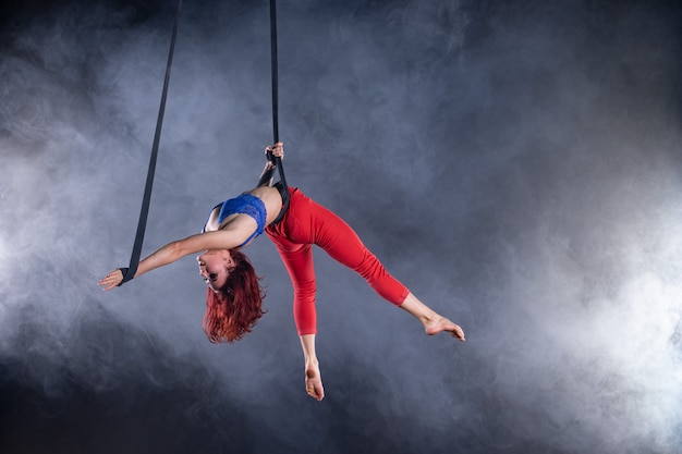 Vrouwelijke atletische, sexy en flexibele luchtfoto circusartiest met roodharige op luchtfoto riemen op zwart.