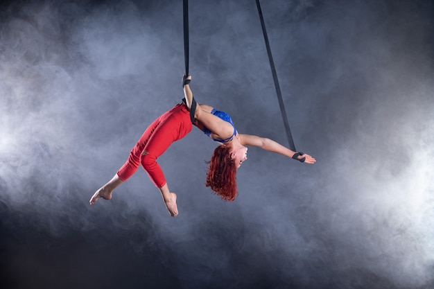 Vrouwelijke atletische, sexy en flexibele luchtfoto circusartiest met roodharige op luchtfoto riemen op zwart.