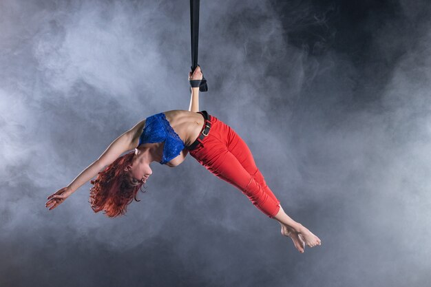 Vrouwelijke atletische, sexy en flexibele luchtfoto circusartiest met roodharige op luchtfoto riemen op zwarte achtergrond.