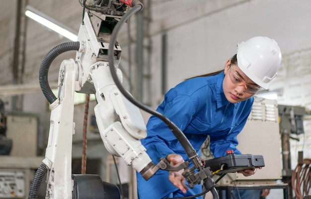 Vrouwelijke automatiseringsingenieur draagt een blauw uniform met veiligheidsinspectie van de helm, een robotarmlasmachine met een systeem op afstand in een industriële fabriek. Kunstmatige intelligentieconcept.