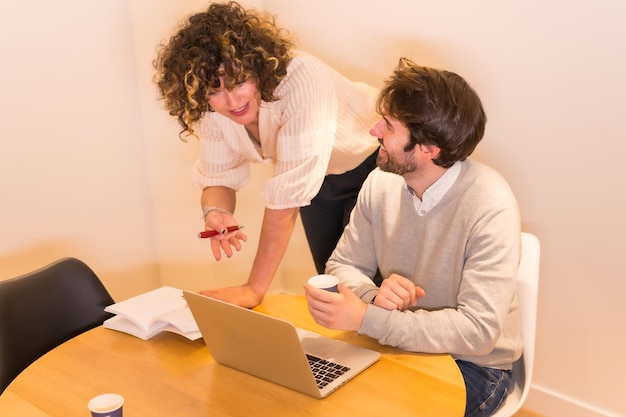 Vrouwelijke baas die de werknemer aanwijzingen geeft aan een tafel op kantoor met een computer en een notitieblok