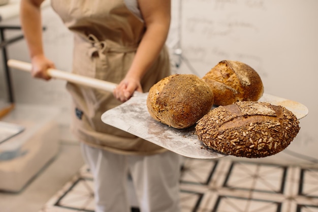 Vrouwelijke bakker die een schil gebruikt om een brood uit de oven in een bakkerij te halen