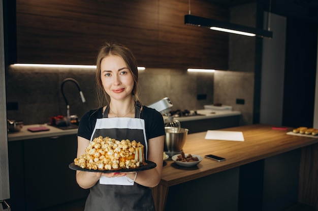 Vrouwelijke bakker met een heerlijke cake De chef-kok houdt een versgebakken cake vast op de achtergrond van de keuken