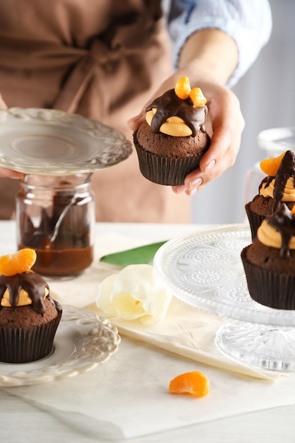 Foto vrouwelijke bakker versierd smakelijke cupcake met een plakje mandarijn en chocolade op de tafel