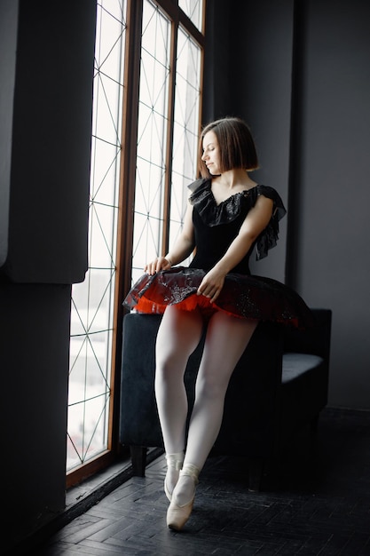 Vrouwelijke balletdanser in zwarte tutu en pointe-schoenen die bij een groot raam staan