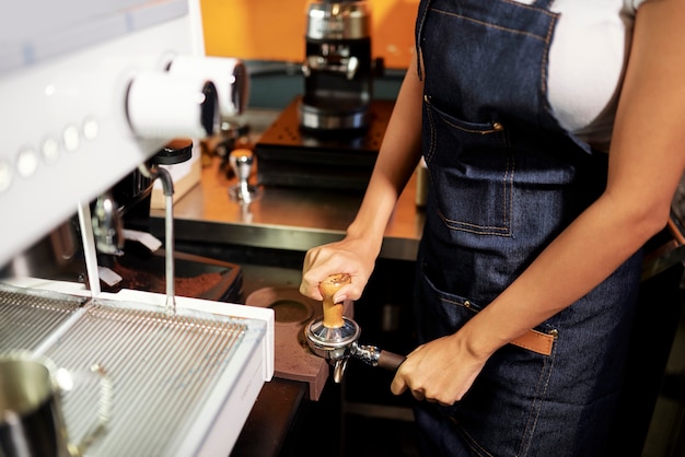 Vrouwelijke barista aanstampen van gemalen koffie