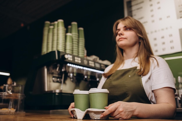 Vrouwelijke barista die koffie geeft in kartonnen bekers