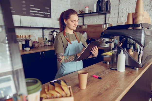 Vrouwelijke barista die op klembord in coffeeshop schrijft