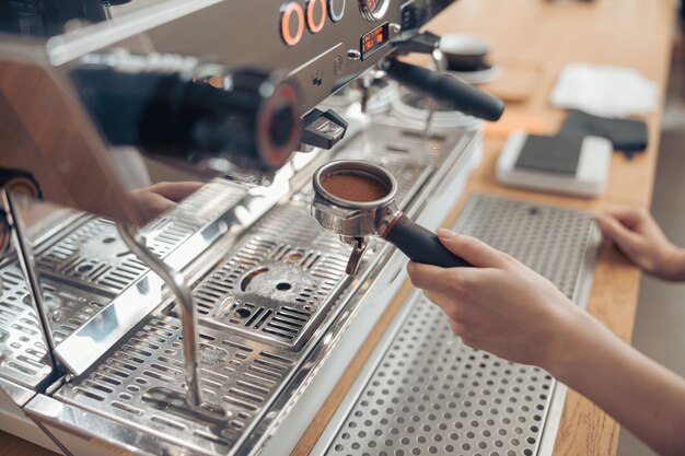 Vrouwelijke barista met behulp van moderne koffiemachine in cafetaria