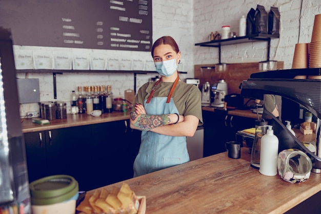 Vrouwelijke barista met medisch masker die in café staat