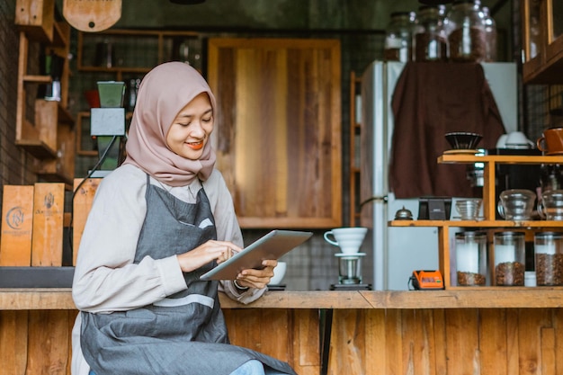 Vrouwelijke barista met sluier die de digitale tablet gebruikt terwijl ze voor de bar zit