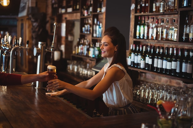 Vrouwelijke barman glas bier geven aan klant